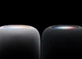 نمای نزدیک از بخش بالایی دو اسپیکر هوشمند HomePod اپل در رنگهای سفید و مشکی با پوشش پارچهای مشبک و سطح لمسی نورانی رنگی در پسزمینه کاملاً سیاه.