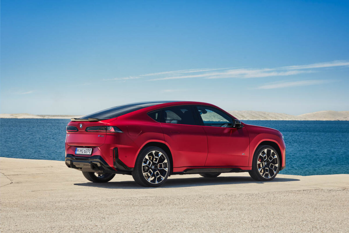 نمای سهرخ عقب خودروی برقی BMW iX4 M60 قرمزرنگ در کنار دریا، با سقف شیبدار، چراغهای کشیده عقب و رینگهای اسپرت