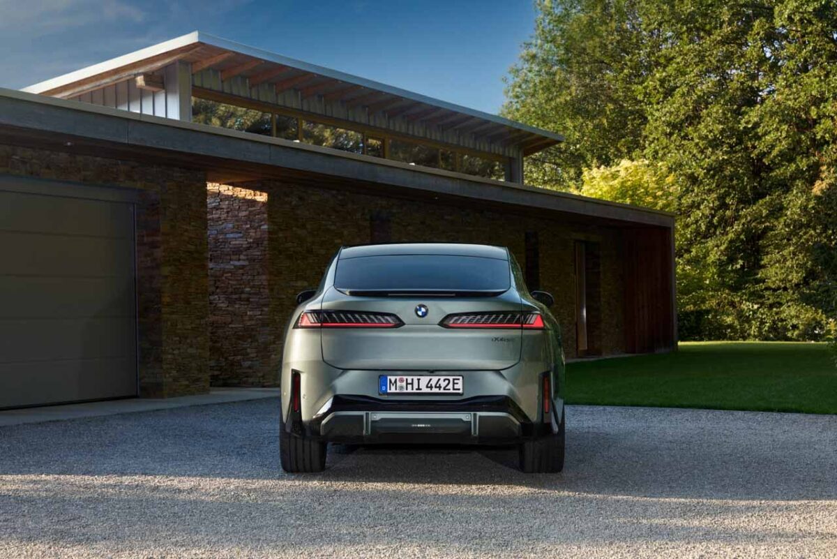 نمای مستقیم عقب BMW iX4 نقرهای با چراغهای LED افقی، نشان BMW و سپر مشکی در محوطه خانهای مدرن