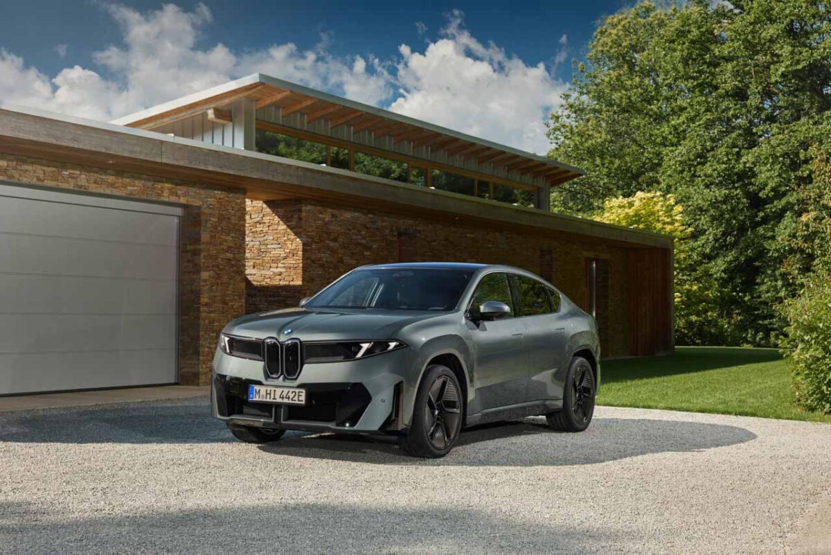 نمای سهرخ جلوی شاسیبلند برقی BMW iX4 نقرهای با جلوپنجره دوگانه، چراغهای LED باریک و سقف کوپه در مقابل خانهای مدرن