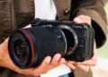 فردی دوربین بدونآینه Canon EOS RV را در دست گرفته و لنزی بزرگ را به بدنه آن متصل میکند