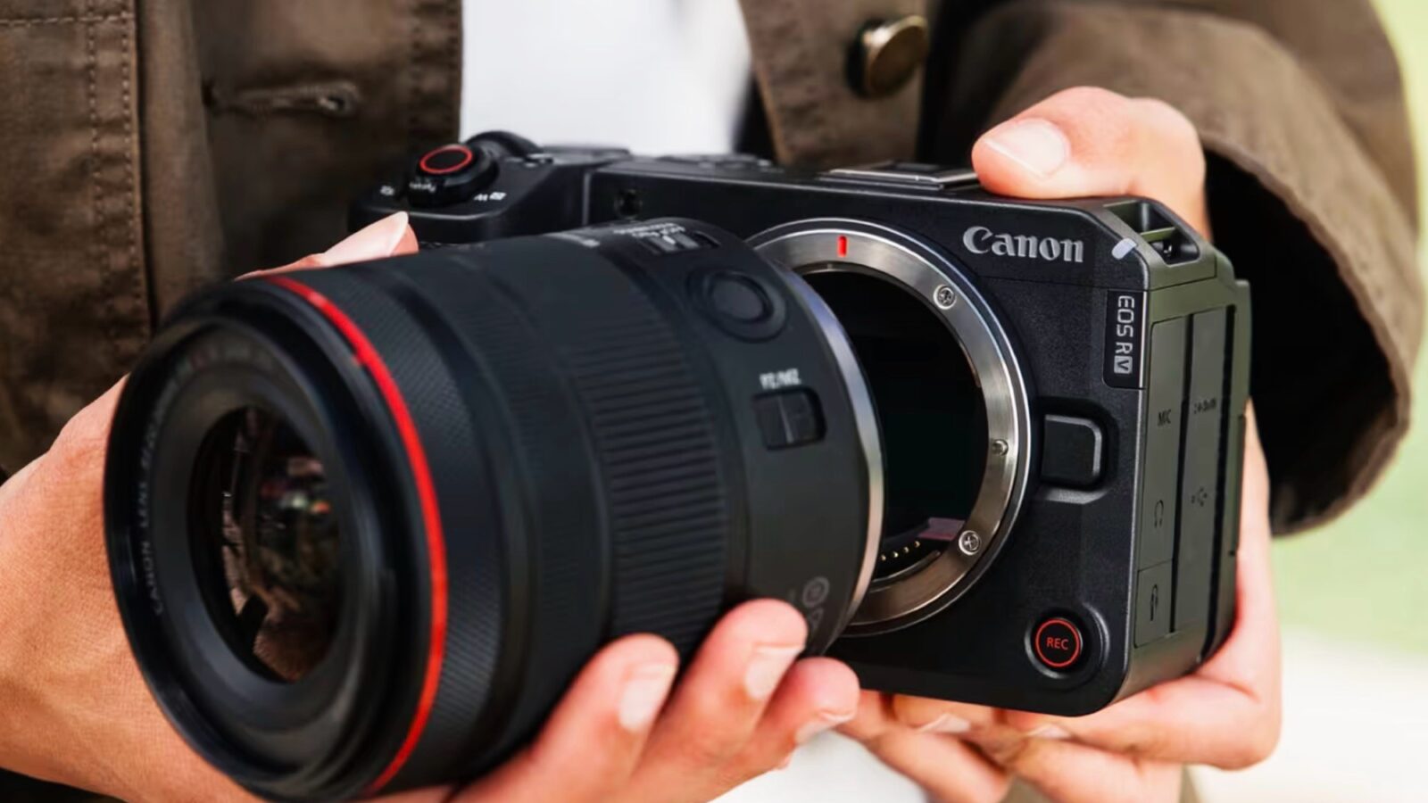 فردی دوربین بدونآینه Canon EOS RV را در دست گرفته و لنزی بزرگ را به بدنه آن متصل میکند