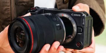 فردی دوربین بدون‌آینه Canon EOS RV را در دست گرفته و لنزی بزرگ را به بدنه آن متصل می‌کند