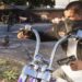 نمای نزدیک از یک موتورسوار در بازی Grand Theft Auto VI که ماسک صورت بر چهره دارد، با یک دست فرمان موتورسیکلت را گرفته و با دست دیگر اسلحه حمل میکند، در حالی که پرندگان در حال پریدن در پیشزمینه هستند.