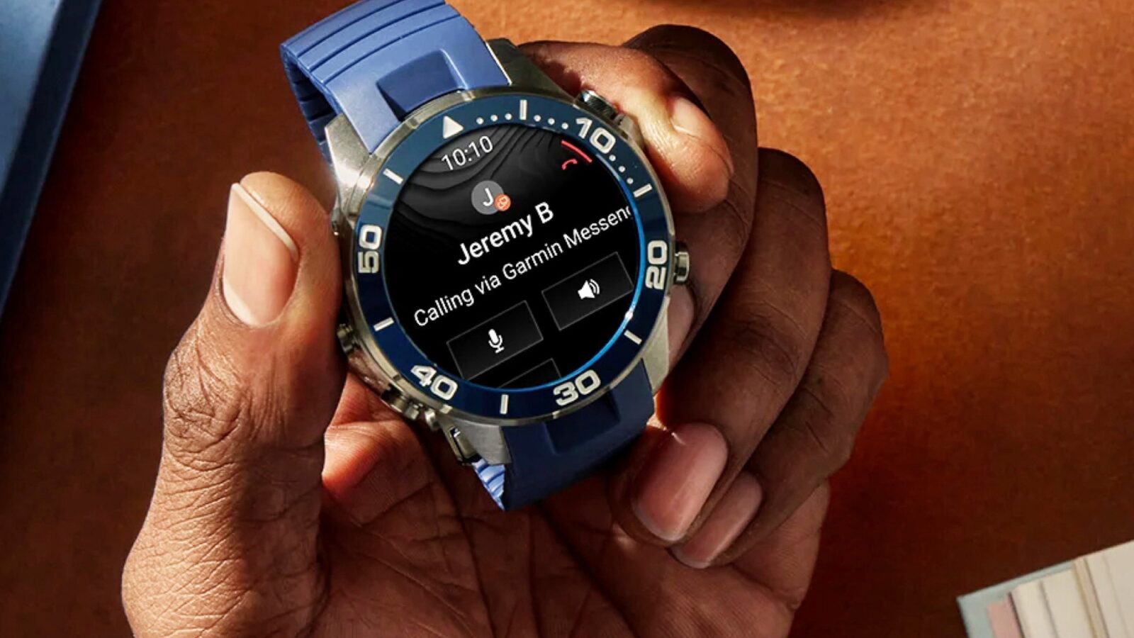 نمای نزدیک از دست فردی که ساعت هوشمند Garmin با بند آبی را نگه داشته و روی صفحه نمایش آن اعلان تماس ورودی از سوی «Jeremy B» با گزینههای پاسخ و رد تماس دیده میشود.