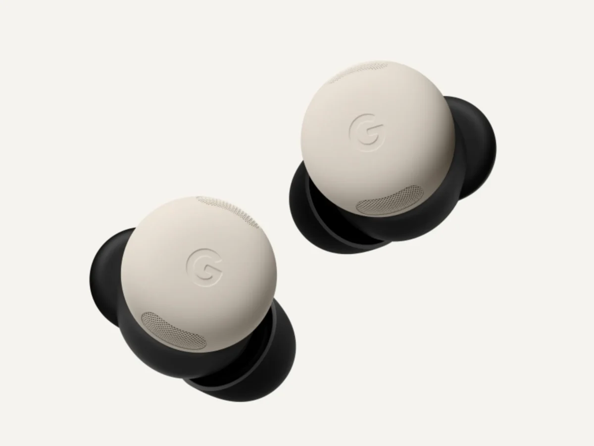 نمای نزدیک محصول از دو ایرباد گوگل Pixel Buds به رنگ کرم روی پس‌زمینه‌ی سفید، با نشان برجسته‌ی گوگل روی سطح فوقانی و بخش‌های مشکی خمیده در پشت