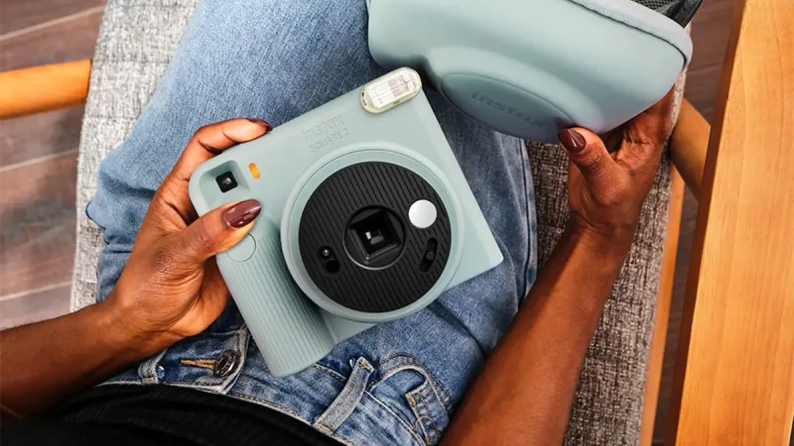 نمای بالای فردی نشسته با شلوار جین آبی که یک دوربین چاپ سریع آبی پاستلی Instax Square SQ2 و کیف محافظ همرنگ آن را روی پای خود نگه داشته است.