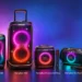 شش اسپیکر بلندگو مهمانی JBL PartyBox با رنگهای مختلف و نورپردازی RGB درخشان در اندازههای گوناگون کنار هم روی پسزمینه گرادیانی بنفش و آبی؛ از راست به چپ مدلهای On-The-Go 2 Plus و On-The-Go 2 و Encore 2 AI Plus و 720 و 130 و 330 با زیرنویس نام هر مدل.
