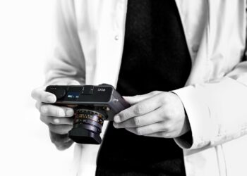 شخصی در حال نگه‌داشتن دوربین عکاسی مدرن Pixii با لنز متصل و نمای سیاه‌وسفید.