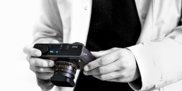 شخصی در حال نگه‌داشتن دوربین عکاسی مدرن Pixii با لنز متصل و نمای سیاه‌وسفید.