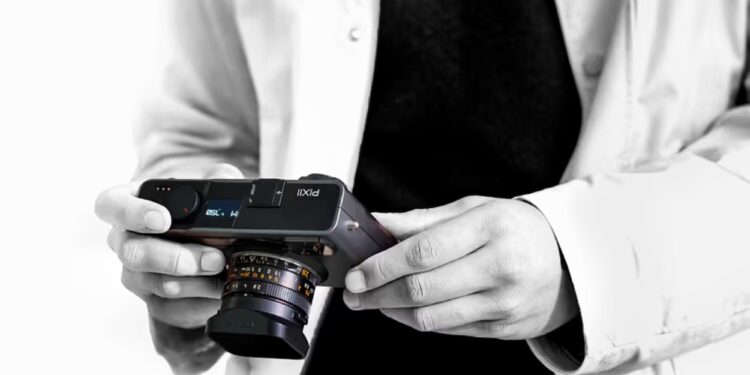 شخصی در حال نگهداشتن دوربین عکاسی مدرن Pixii با لنز متصل و نمای سیاهوسفید.
