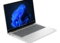 لپ‌تاپ نقره‌ای رنگ HP ProBook روی میز با صفحه‌نمایش روشن و تصویر زمینه موج‌های آبی رنگ ویندوز ۱۱.