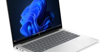 لپتاپ نقرهای رنگ HP ProBook روی میز با صفحهنمایش روشن و تصویر زمینه موجهای آبی رنگ ویندوز ۱۱.