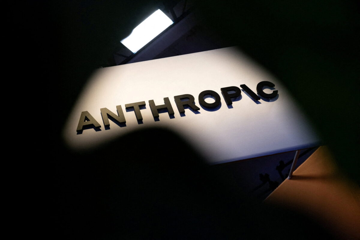 نمای نزدیک از تابلوی برجسته با نام شرکت Anthropic با حروف مشکی روی زمینهای سفید و منحنی در اتاقی تاریک که با نورپردازی روشن شده است.