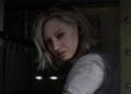 نمای نزدیک از شخصیت زن Resident Evil Requiem با موهای کوتاه و روشن و چشمان خاکستری که رو به دوربین نگاه می‌کند؛ او پیراهن سفید آلوده‌ای بر تن دارد و در پس‌زمینه‌ی تاریک، فضای داخلی متروکه‌ای دیده می‌شود