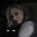 نمای نزدیک از شخصیت زن Resident Evil Requiem با موهای کوتاه و روشن و چشمان خاکستری که رو به دوربین نگاه میکند؛ او پیراهن سفید آلودهای بر تن دارد و در پسزمینهی تاریک، فضای داخلی متروکهای دیده میشود