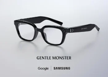 عینک هوشمند مشکی رنگ با دوربین روی دسته، بالای نوشته Gentle Monster و همکاری مشترک Google و Samsung روی پس‌زمینه خاکستری روشن.