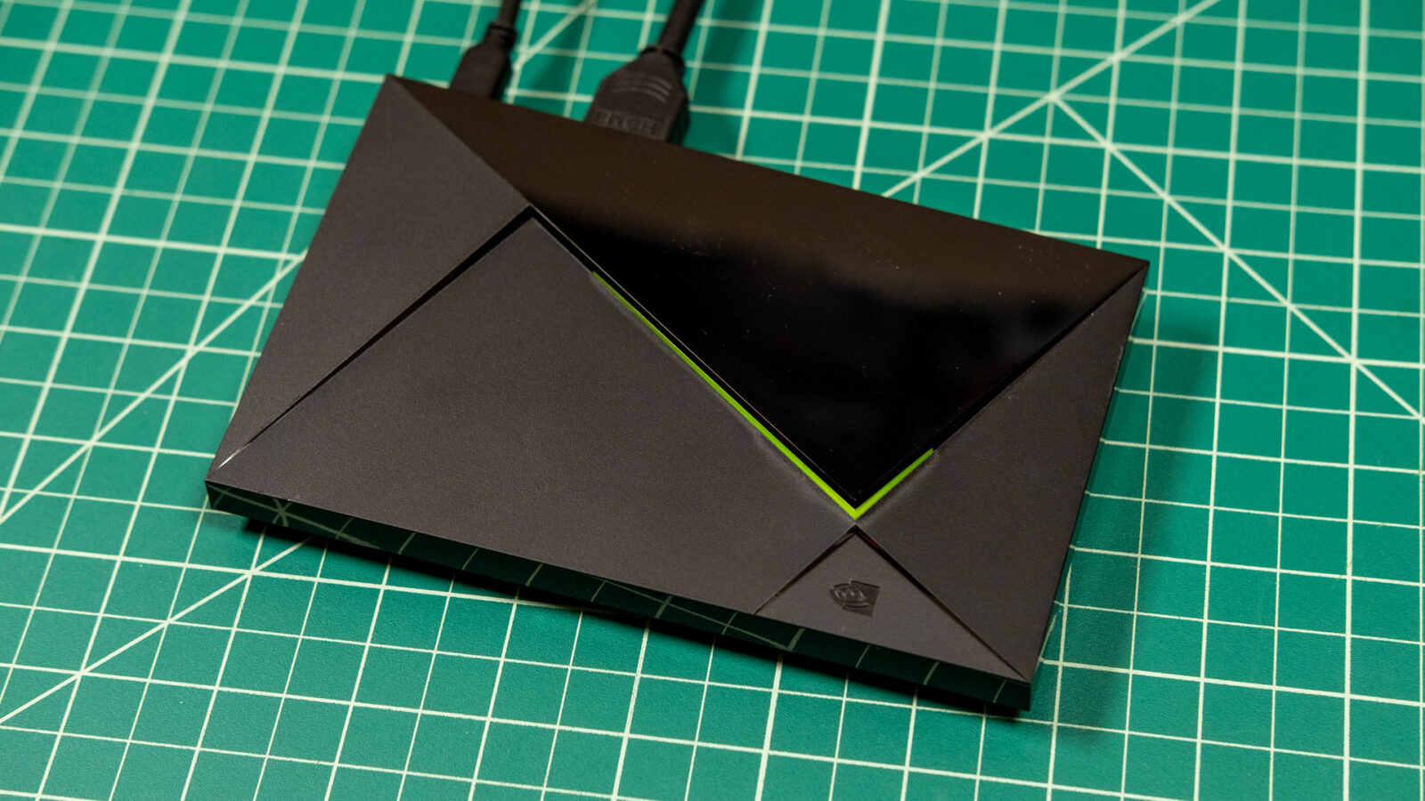 تی‌وی باکس Nvidia Shield TV Pro با بدنه مشکی، طراحی زاویه‌دار و خط نورانی سبز روی صفحه کار مدرج سبز