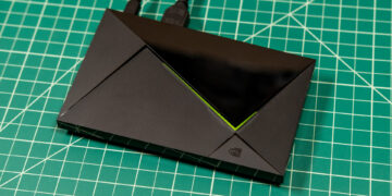تیوی باکس Nvidia Shield TV Pro با بدنه مشکی، طراحی زاویهدار و خط نورانی سبز روی صفحه کار مدرج سبز