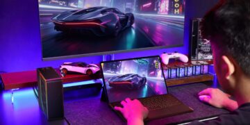 گیمری پشت میز کار که مشغول اجرای بازی ریسینگ سایبرپانکی روی تبلت Onexplayer متصل به مانیتور گیمینگ عریض، پردازنده گرافیکی اکسترنال و کیبورد است.
