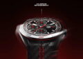 نمای نزدیک ساعت هوشمند TAG Heuer Connected Calibre E5 با عقربهها و نشانگرهای قرمز مسابقهای، قاب سرامیکی و بند با بافت فیبر کربن و دوخت قرمز، روی پسزمینهای با تم تیره و قرمز حرکت دورانی دارد.