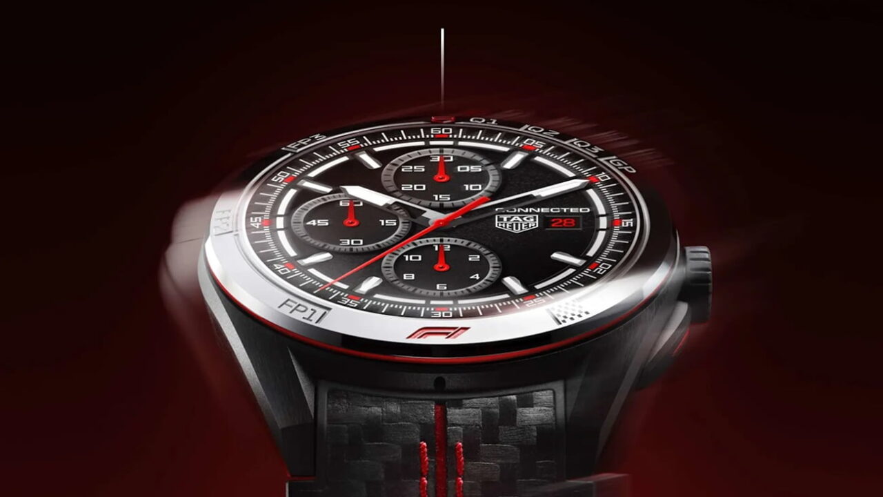 نمای نزدیک ساعت هوشمند TAG Heuer Connected Calibre E5 با عقربهها و نشانگرهای قرمز مسابقهای، قاب سرامیکی و بند با بافت فیبر کربن و دوخت قرمز، روی پسزمینهای با تم تیره و قرمز حرکت دورانی دارد.