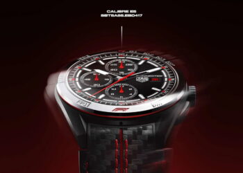 نمای نزدیک ساعت هوشمند TAG Heuer Connected Calibre E5 با عقربه‌ها و نشانگرهای قرمز مسابقه‌ای، قاب سرامیکی و بند با بافت فیبر کربن و دوخت قرمز، روی پس‌زمینه‌ای با تم تیره و قرمز حرکت دورانی دارد.