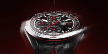 نمای نزدیک ساعت هوشمند TAG Heuer Connected Calibre E5 با عقربه‌ها و نشانگرهای قرمز مسابقه‌ای، قاب سرامیکی و بند با بافت فیبر کربن و دوخت قرمز، روی پس‌زمینه‌ای با تم تیره و قرمز حرکت دورانی دارد.