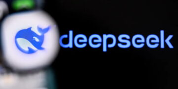 نمای نزدیک و تار از صفحه گوشی هوشمند که لوگو و نام آبی‌رنگ دیپ‌سیک (DeepSeek) را بر روی پس‌زمینه مشکی نمایش می‌دهد.