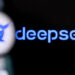 نمای نزدیک و تار از صفحه گوشی هوشمند که لوگو و نام آبیرنگ دیپسیک (DeepSeek) را بر روی پسزمینه مشکی نمایش میدهد.