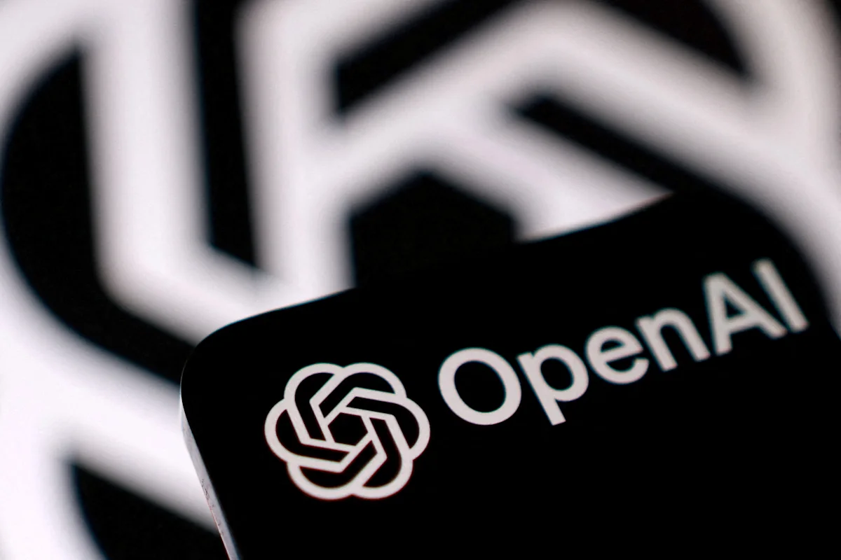 عکس نزدیک از یک کارت با پسزمینه مشکی که لوگو و نام OpenAI با رنگ سفید روی آن چاپ شده و در گوشه پایین آن نشان گلگشتی ششپره این شرکت قرار دارد. در پسزمینه، همان لوگوی بزرگ و تارشده با نور سفید روی پسزمینه مشکی دیده میشود