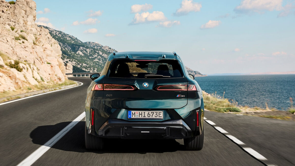 نمای عقب شاسیبلند برقی BMW iX3 M60 xDrive سبز تیره با چراغهای LED باریک و طراحی اسپرت در جادهای ساحلی و کوهستانی