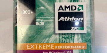 عکس بستهبندی قدیمی پردازنده AMD: نمای نزدیک از جعبه پلاستیکی پردازنده AMD Athlon XP با مدل 1800+ که روی آن لوگوی مشکی AMD Athlon، نوار نارنجی رنگ با عبارت «EXTREME PERFORMANCE» و برچسب «for Windows XP» روی پسزمینه سبز و موجدار دوران اوایل دهه ۲۰۰۰ دیده میشود.