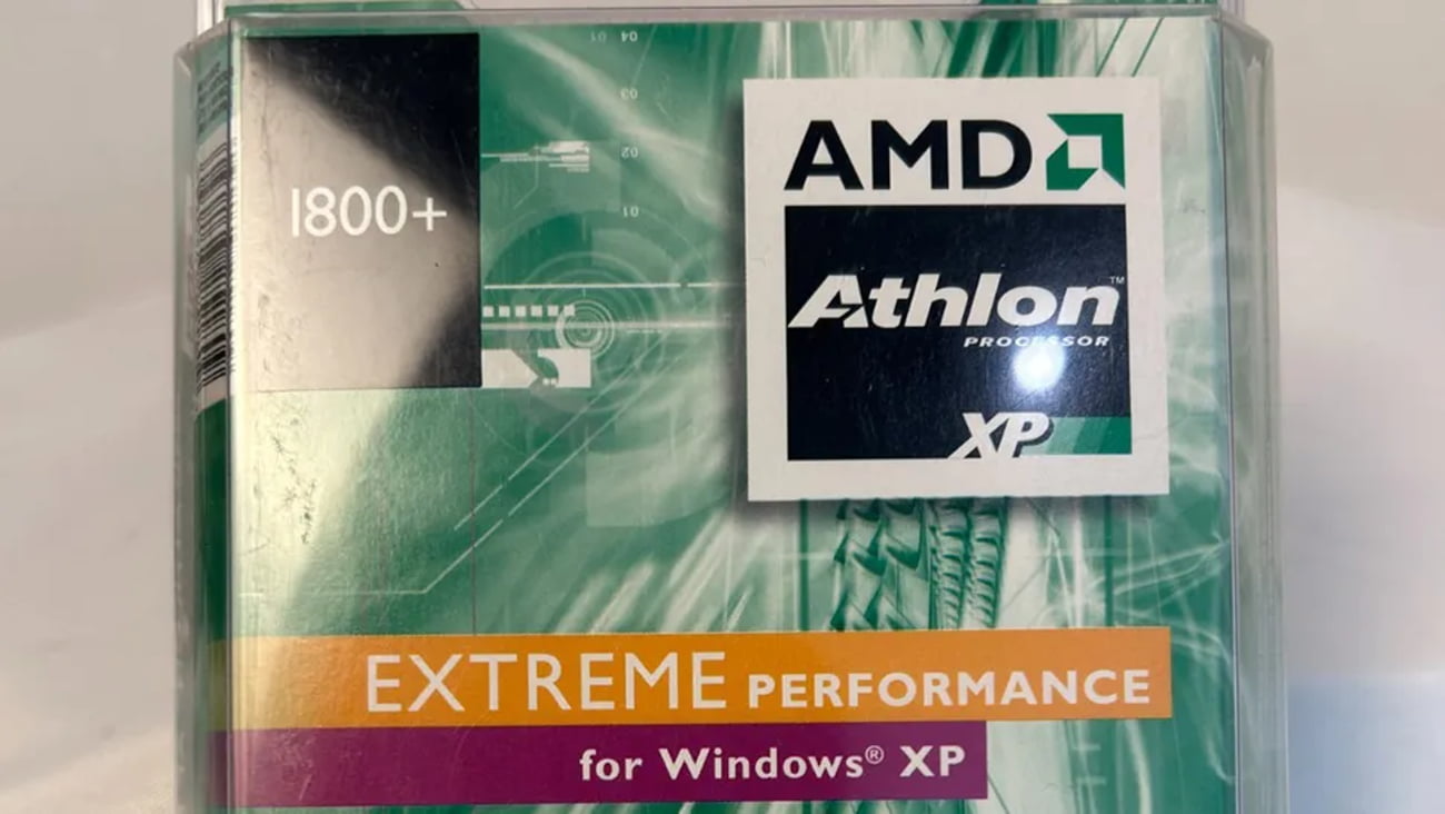 عکس بستهبندی قدیمی پردازنده AMD: نمای نزدیک از جعبه پلاستیکی پردازنده AMD Athlon XP با مدل 1800+ که روی آن لوگوی مشکی AMD Athlon، نوار نارنجی رنگ با عبارت «EXTREME PERFORMANCE» و برچسب «for Windows XP» روی پسزمینه سبز و موجدار دوران اوایل دهه ۲۰۰۰ دیده میشود.