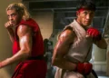 دو مبارز فیلم Street Fighter با لباسهای سنتی قرمز و سفید در حالت رزمی و پشت به یکدیگر در یک سالن تمرینی ایستادهاند.