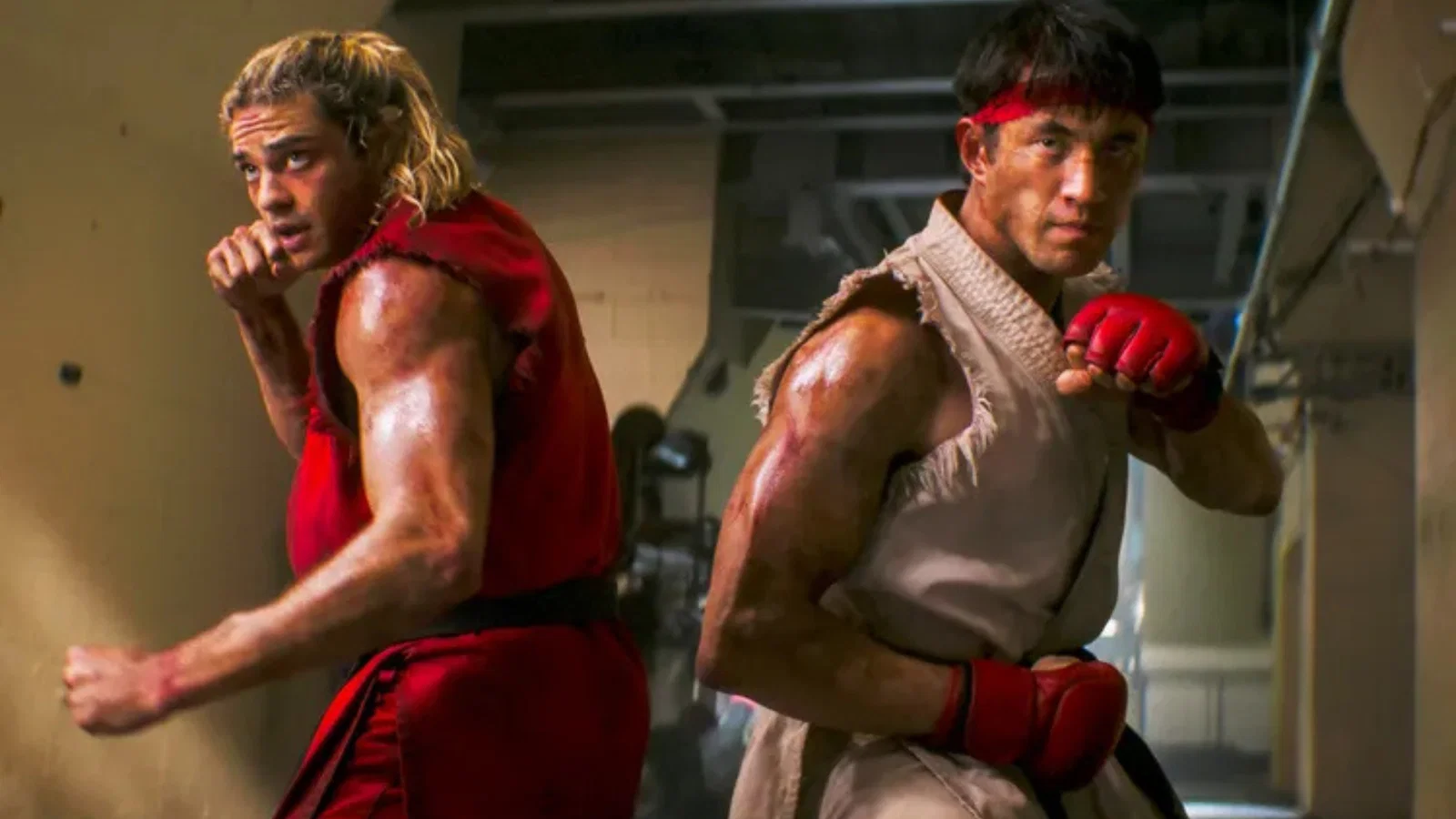 دو مبارز فیلم Street Fighter با لباسهای سنتی قرمز و سفید در حالت رزمی و پشت به یکدیگر در یک سالن تمرینی ایستادهاند.