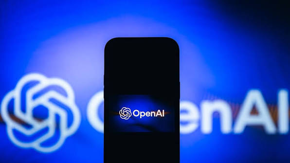 گوشی هوشمند در نمای روبهرو با صفحه سیاه که لوگوی درخشان OpenAI روی نمایشگر آن باز شده و در پسزمینهای با نور آبی عریض قرار دارد.